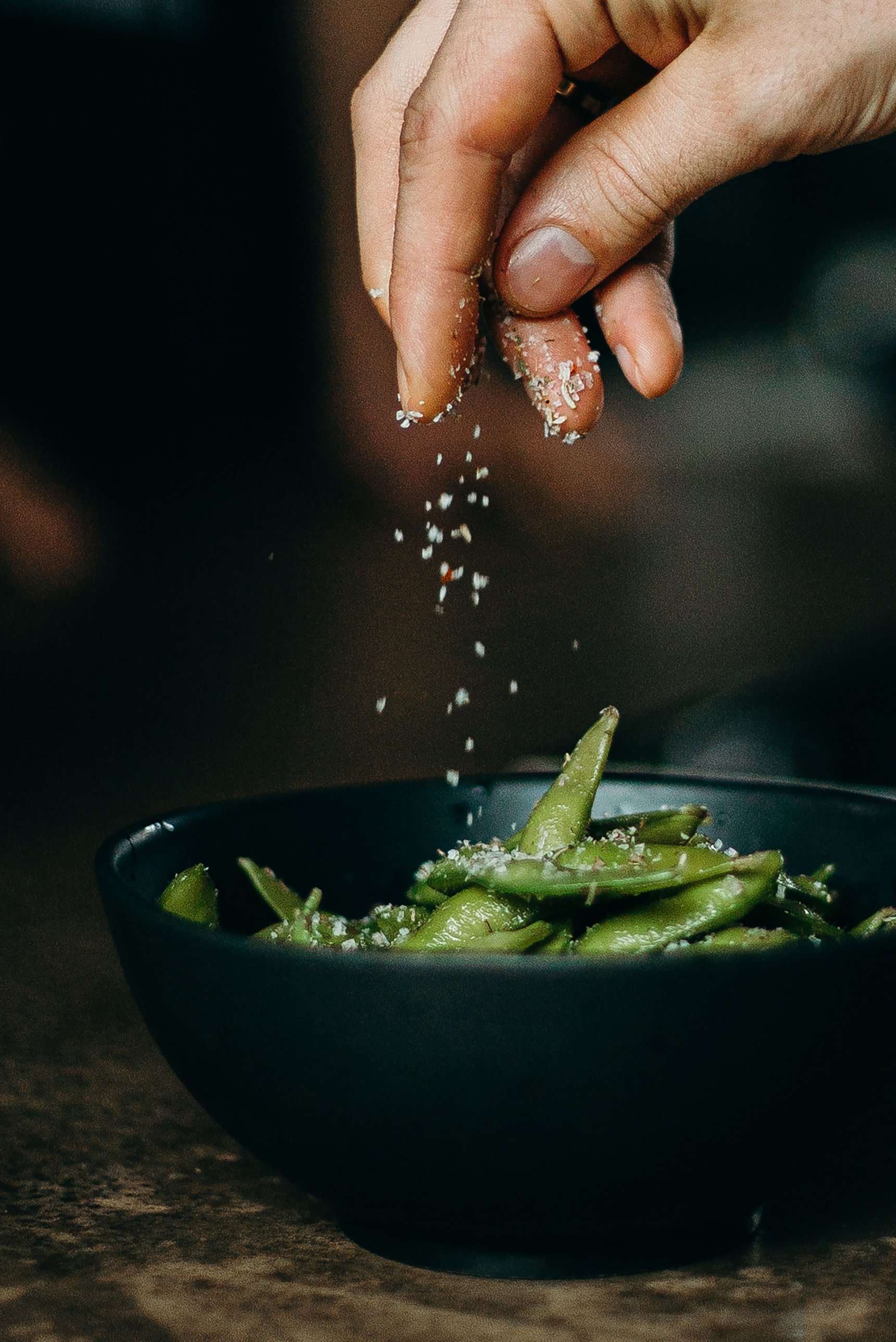 A cook seasoning a bowl of edamame by hand